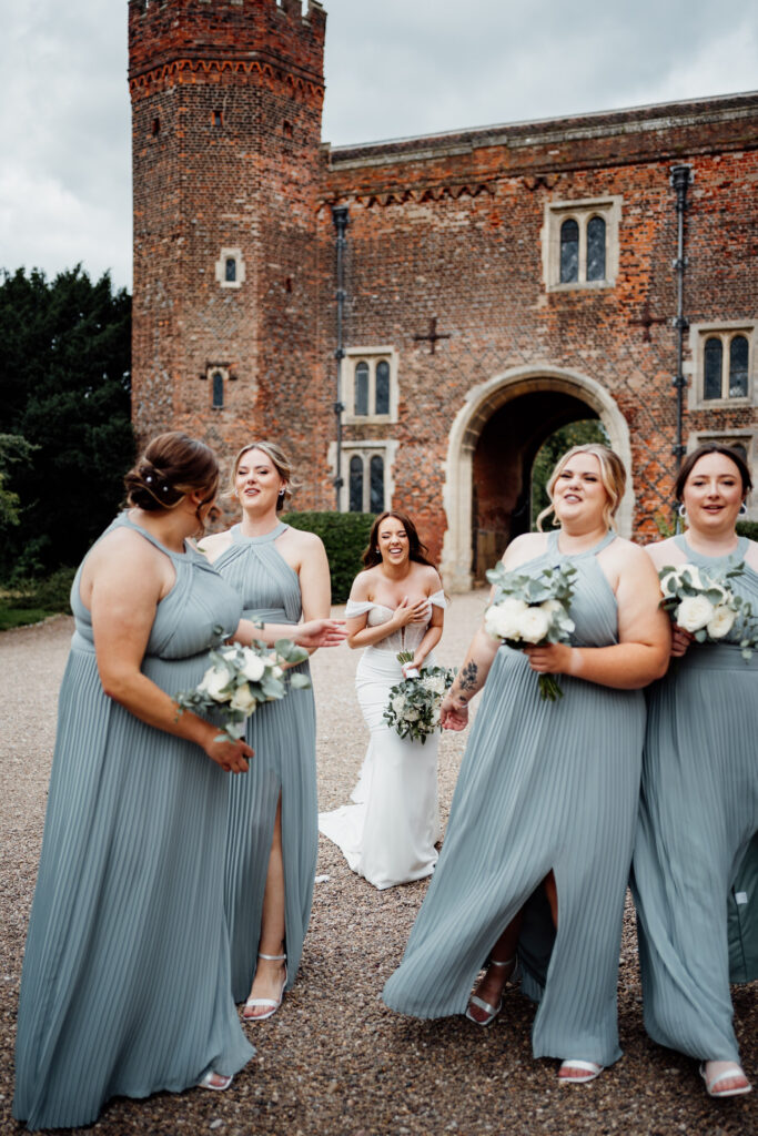 Bride and bridesmaids laugh in front of Tudor tower at Hodsock Priory