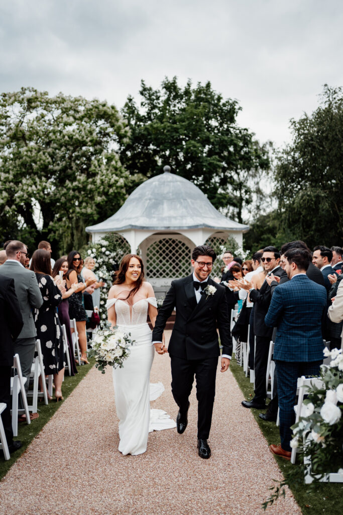 Bride and groom walking down aisle of outdoor ceremony area at Hodsock Priory