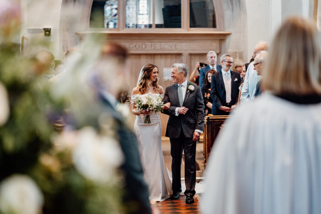 bride walking down aisle with father as they smile at each other