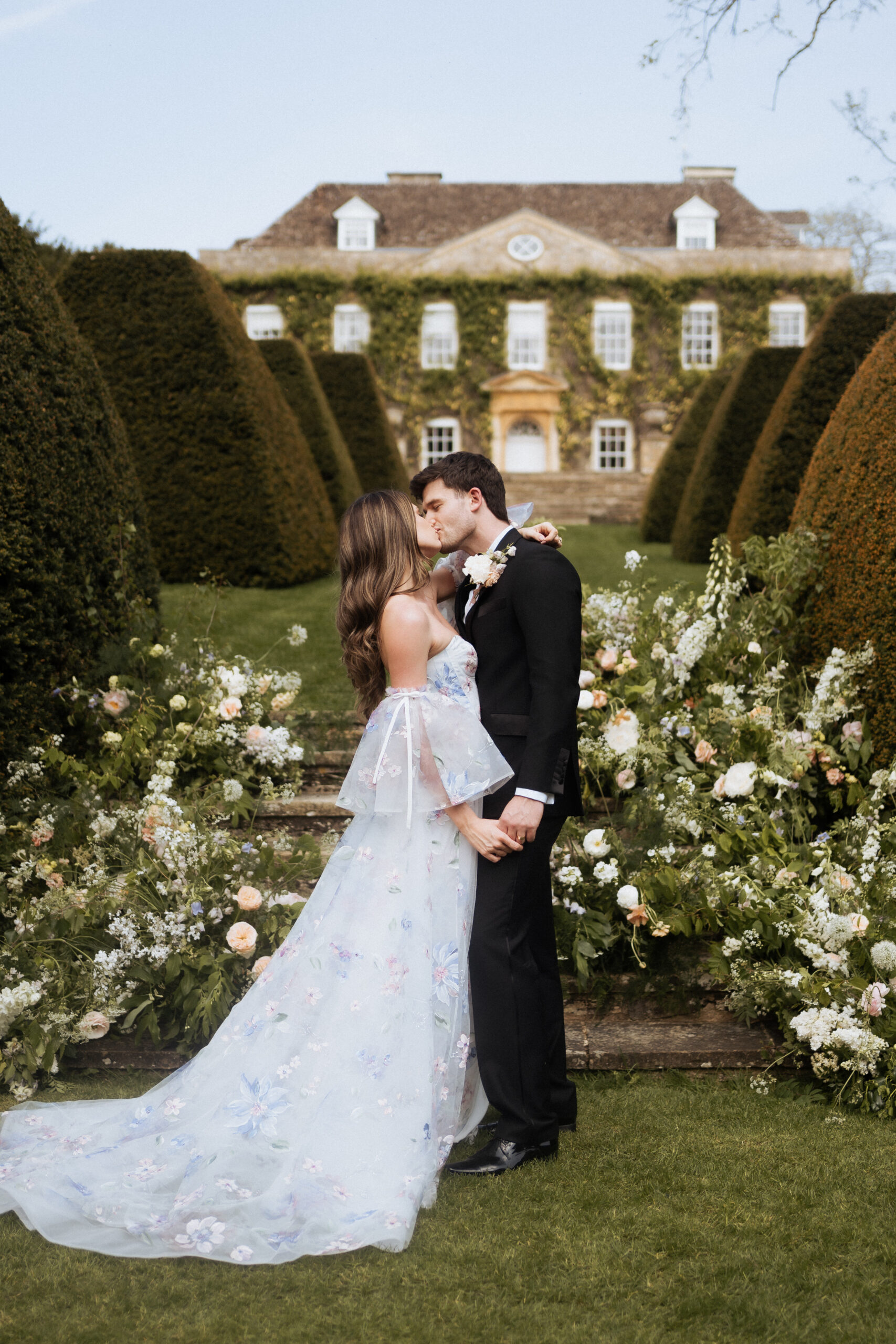 Bride and groom kiss during the ceremony of their wedding, Cornwell Manor in the background