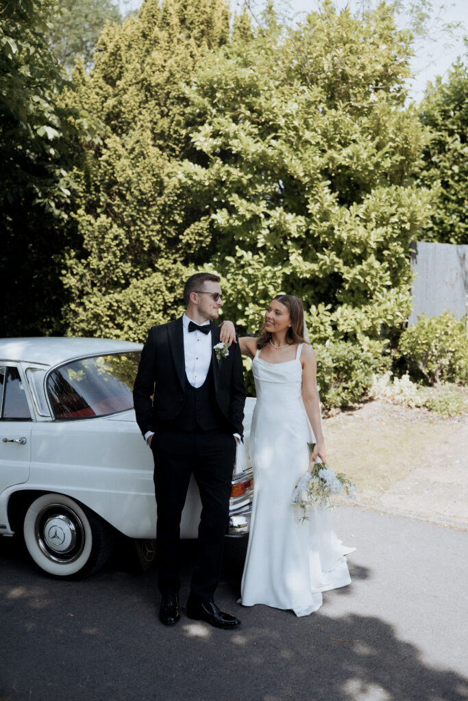 Bride and groom posing in front of classic Mercedes car